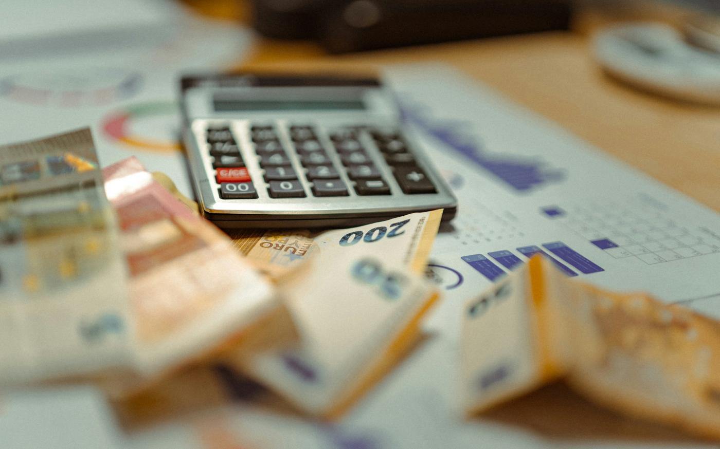 A calculator sitting on top of a pile of money by Jakub Żerdzicki courtesy of Unsplash.